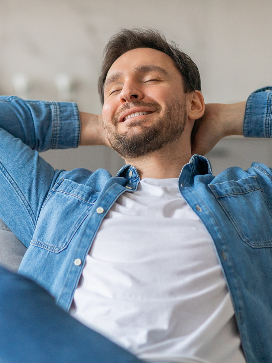 A man in a blue shirt leaning back on a couch